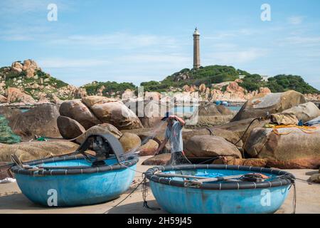 Un pescatore locale svella la rete di pesca sulla riva del mare. Spiaggia pittoresca con grandi rocce. Vecchio faro si trova in lontananza. Alta qualità Foto Stock