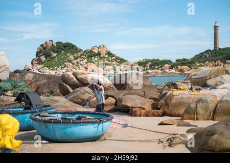 Un pescatore locale svella la rete di pesca sulla riva del mare. Spiaggia pittoresca con grandi rocce. Vecchio faro si trova in lontananza. Alta qualità Foto Stock