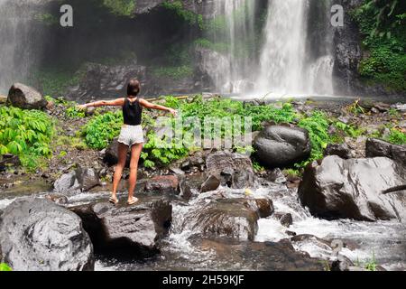 una giovane ragazza in piedi sulle rocce ammira la cascata naturale. la vista dal retro Foto Stock
