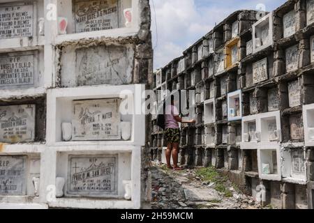 Una donna offre candele mentre la gente visita un cimitero pubblico in osservanza di All Souls’ Day a Quezon City, Metro Manila, Filippine. Foto Stock