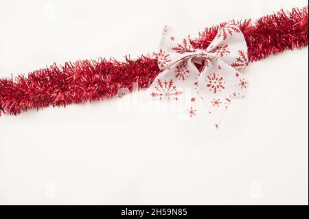 Arco decorativo natalizio e tinsel rosso su sfondo bianco Foto Stock