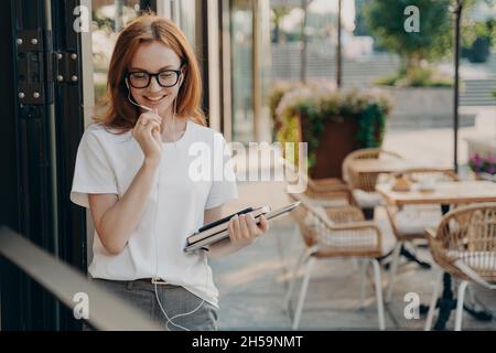 Bella donna rossa giovane fa chiamata a distanza utilizza auricolari con microfono Foto Stock