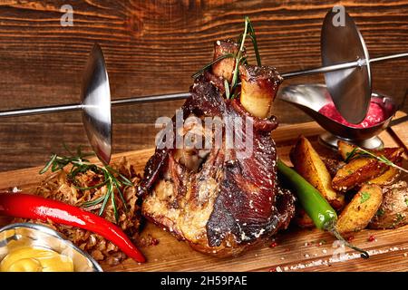 nocciole di maiale arrosto eisbein con cavolo bollito brasato, patate, peperoncini e senape su tagliere di legno. Serve un pasto pronto in un ristorante Foto Stock