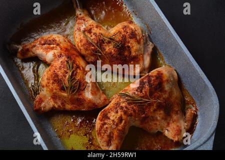 Quarti di coscia di pollo al forno e bastoncini di drumstick conditi con aglio ed erbe in un piatto da forno Foto Stock