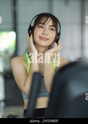 Affascinante donna fitness che ascolta la musica tramite le cuffie wireless mentre si allenano sul tapis roulant. Foto Stock