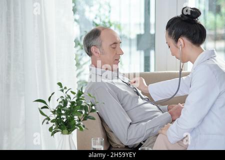 Giovane medico generale femminile che ascolta il respiro dell'uomo anziano con stetoscopio Foto Stock