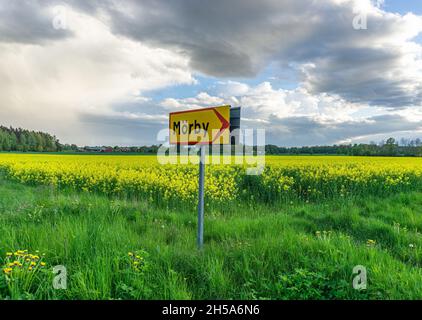 Vadstena, Svezia - 23 maggio 2021: Campo di colza in background e in primo piano un cartello stradale con la direzione per il villaggio di Morby Foto Stock