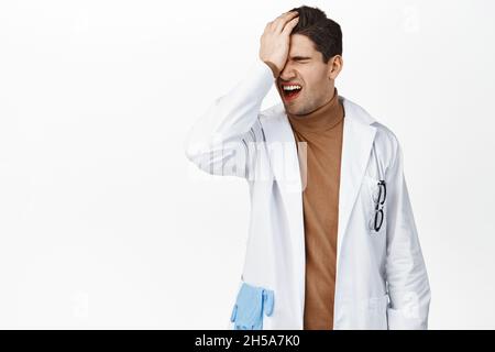 Il facepalm medico frustrato, deluso in smth, facendo il cattivo errore, in piedi sconvolto contro sfondo bianco, indossando uniforme medica Foto Stock