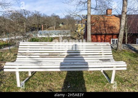 Stoccolma, Svezia - 6 aprile 2021: Un'ombra di persona che rimane di fronte alla panchina bianca Foto Stock