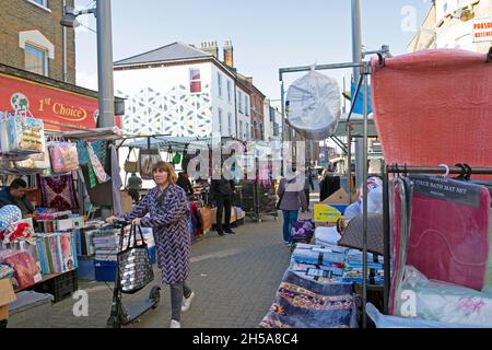 Donna che spinge scooter oltre il mercato bancarelle poche persone che camminano lungo Walthamstow mercato di High Street commercianti in autunno ottobre 2021 Londra UK KATHY DEWITT Foto Stock