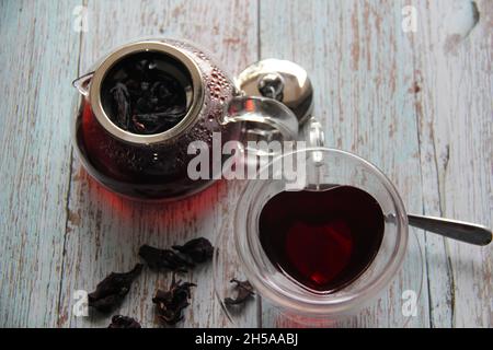 Tè Hibiscus : in una tazza a forma di cuore con una teiera di vetro trasparente su un tavolo di legno. Vista dall'alto. Foto Stock