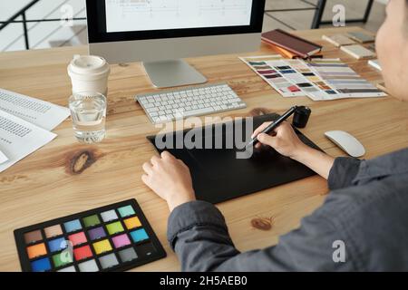 Mani di giovane designer femminile con penna stilo e tavoletta grafica disegno schizzo sullo schermo del computer mentre si siede da tavolo Foto Stock