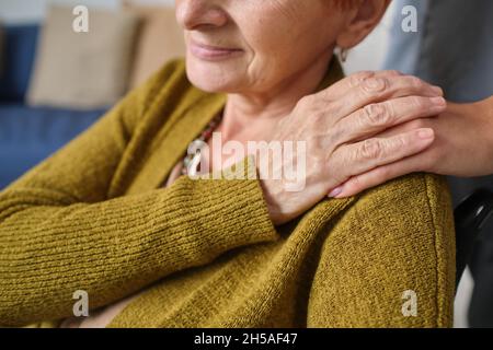 Primo piano di una donna anziana che tiene una mano di infermiere mentre la prende in sedia a rotelle Foto Stock