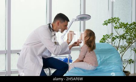 Il paziente figlio visita l'ufficio medico. Il medico ascolta i polmoni del bambino con uno stetoscopio, parla con la bambina. Foto Stock