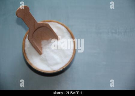 Sale, bianco, raffinato, in una ciotola di legno, con un misurino di legno su un vecchio tavolo di legno. Vista dall'alto. Foto Stock