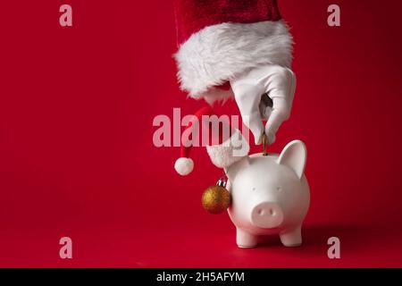 Babbo Natale mettere soldi in una scatola di soldi della banca del piggy di Natale. Concetto di risparmio festivo Foto Stock