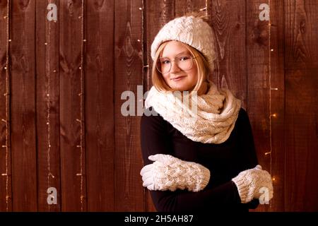 Ritratto bella ragazza con capelli corti in cappello a maglia e guanti caldi su sfondo di legno Foto Stock