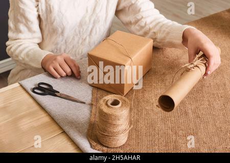 Donna caucasica in confezione bianca con maglione a maglia. Concentratevi sulle mani. Carta da imballaggio artigianale e spago naturale. Riciclaggio del materiale. Buone vacanze pres Foto Stock