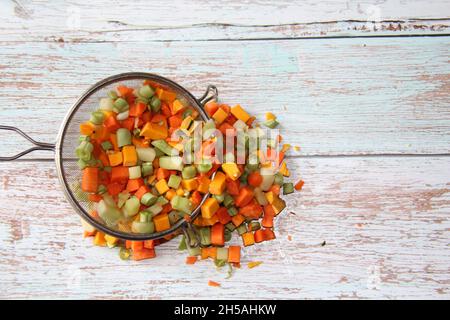 Ortaggi e legumi: Zucca, fagioli verdi, carote e chayote, tagliati molto piccoli, in un setaccio di metallo su una vecchia tavola di legno. Vista dall'alto. Foto Stock