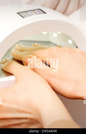 Mano femminile con le dita curate asciugate all'interno della macchina UV in salone manicure Foto Stock