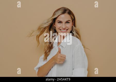 Eccitata bella donna bionda in posa in studio con pollice su ok segno Foto Stock