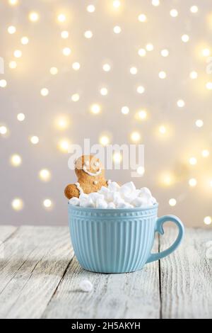 uomo di pan di zenzero in una tazza blu di bevanda calda invernale con marshmallows su sfondo bianco di legno. Sfondo natalizio. Tradizionale atmos di Natale Foto Stock