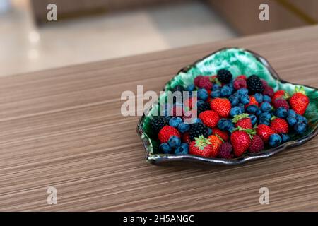 Piatto di design con lamponi freschi, more, mirtilli, fragole su un letto. Colazione sana. Messa a fuoco selettiva morbida, rumore artistico. Foto Stock