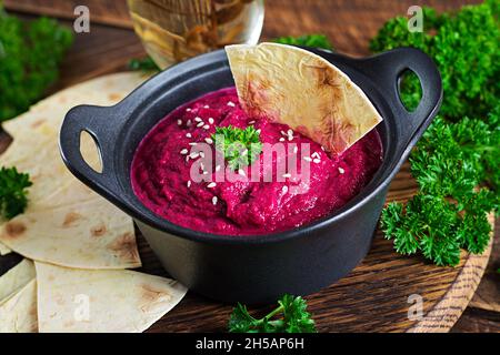 Hummus di barbabietola arrosto con pita in una ciotola nera su sfondo di legno. Foto Stock