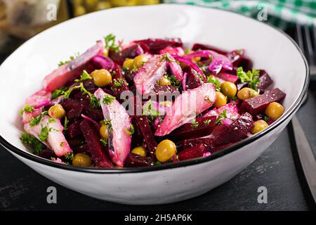 Insalata con aringhe, piselli verdi e barbabietole ripieni di olio vegetale su tavola scura. Foto Stock