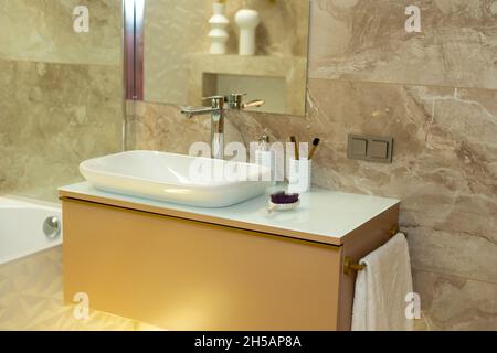 Bagno moderno in tonalità beige con piastrelle di marmo e lavandino bianco. Design degli interni. Messa a fuoco selettiva morbida, rumore artistico Foto Stock