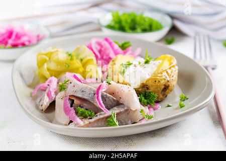 Aringhe con patate al forno, cipolle e cetrioli sottaceto su un piatto. Cucina tradizionale. Foto Stock