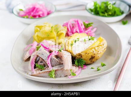 Aringhe con patate al forno, cipolle e cetrioli sottaceto su un piatto. Cucina tradizionale. Foto Stock