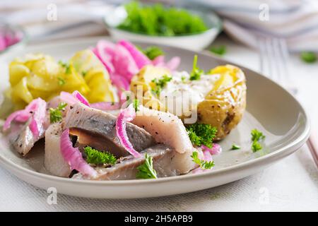 Aringhe con patate al forno, cipolle e cetrioli sottaceto su un piatto. Cucina tradizionale. Foto Stock