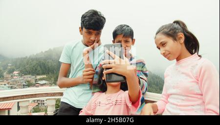 Quattro piccoli fratelli indiani che prendono un selfie all'aperto in una giornata di sole Foto Stock