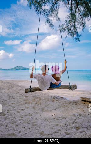 Bang Tao Beach Phuket Thailandia, spiaggia con palme e un uomo e una coppia di donne nell'altalena sulla spiaggia. Concetto di estate, viaggio, vacanza e vacanza - Swing appende da palme da cocco Foto Stock