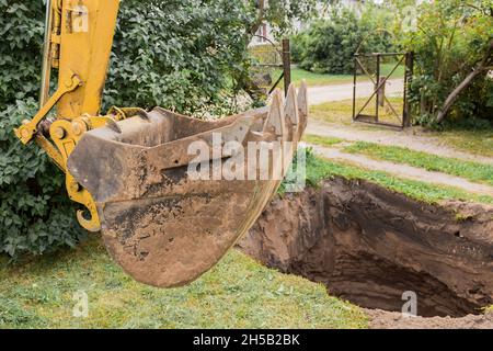 Una benna di un bulldozer o un escavatore con un mucchio di sabbia e terra sullo sfondo di scavi di costruzione industriale. Foto Stock