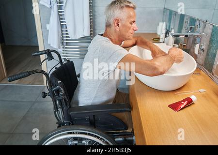 Uomo anziano con disabilità fisica che pulisce le mani nel lavandino Foto Stock