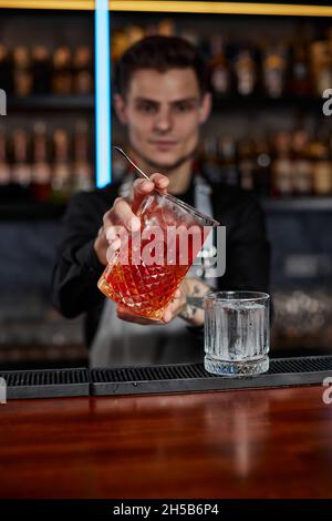 il barman in grembiule versa un cocktail vecchio stile in un bicchiere Foto Stock