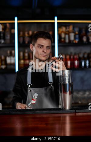 Il barista in grembiule aggiunge l'ingrediente allo shaker Foto Stock
