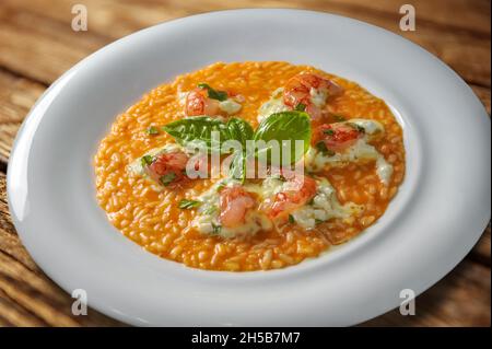 Risotto con salsa di pomodoro con gamberi rossi Mazara del Vallo, burrata di mozzarella e foglie di basilico, in piatto bianco su tavola di legno Foto Stock