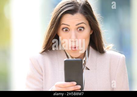 Il ritratto della vista frontale di un dirigente sorpreso sta controllando il contenuto dello smartphone nella strada Foto Stock