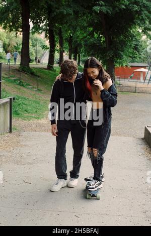 Ragazzo adolescente che insegna lo skateboard a un amico femminile nel parco Foto Stock