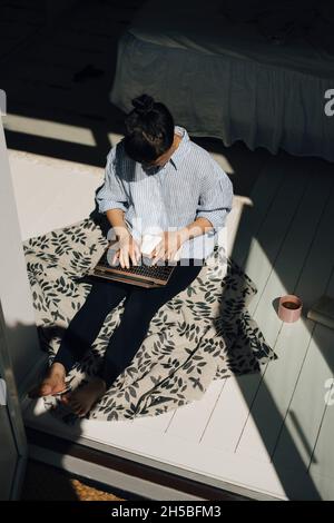 Visualizzazione ad angolo elevato della freelance femminile utilizzando un computer portatile in camera da letto a casa Foto Stock