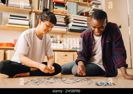 Coppia sorridente che gioca a puzzle sul pavimento a casa Foto Stock