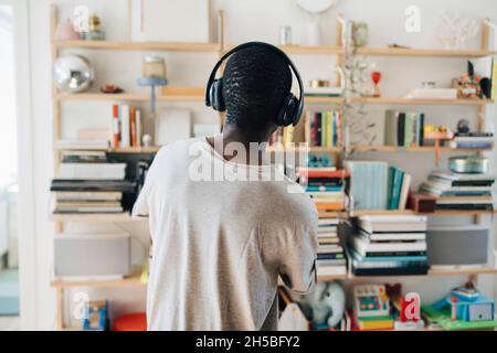 Vista posteriore dell'uomo adulto medio che ascolta la musica attraverso le cuffie a casa Foto Stock