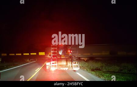 Camion traino di un rimorchio in attesa di un attraversamento ferroviario di notte Foto Stock