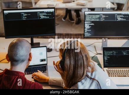 Visualizzazione ad angolo elevato di hacker maschi e femmine che codificano su laptop in ufficio Foto Stock