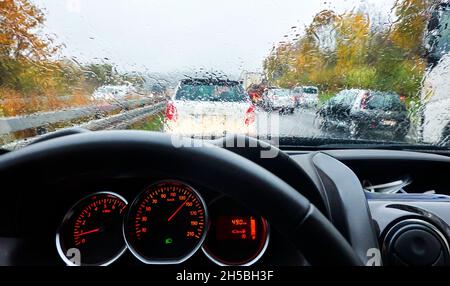 Vista sul cruscotto di un'auto attraverso il parabrezza bagnato dalla pioggia del traffico sull'autobahn in Germania Foto Stock