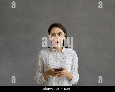 Donna frustrata e arrabbiata con espressione facciale insoddisfatta si leva in piedi con il telefono nelle mani. Foto Stock