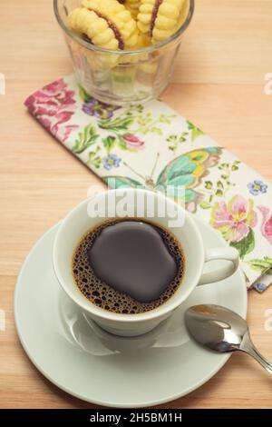 Una tazza di caffè con un mucchio di biscotti al burro cosparsi di zucchero su una superficie di legno. Foto Stock